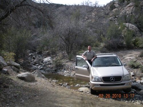 Niel Malan posing in a 4-wheel drive car stopped in creek bed.